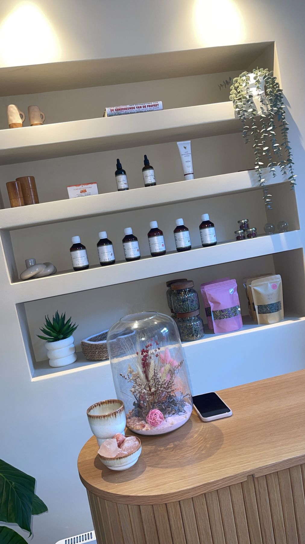 Planken in de ontvangstruimte met flesjes, theezakken en een glazen stolp met gedroogde bloemen